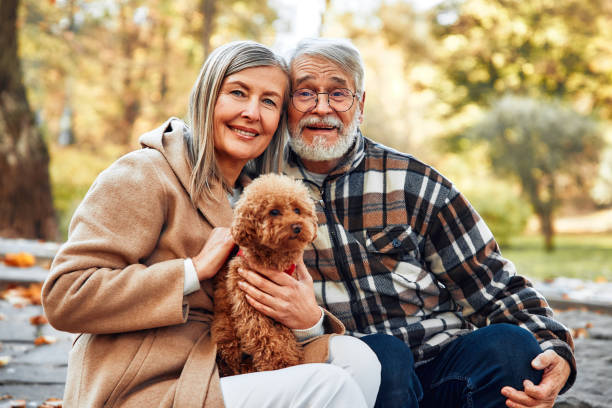 Mature beautiful gray-haired couple walking with their dog friend in the park in autumn.